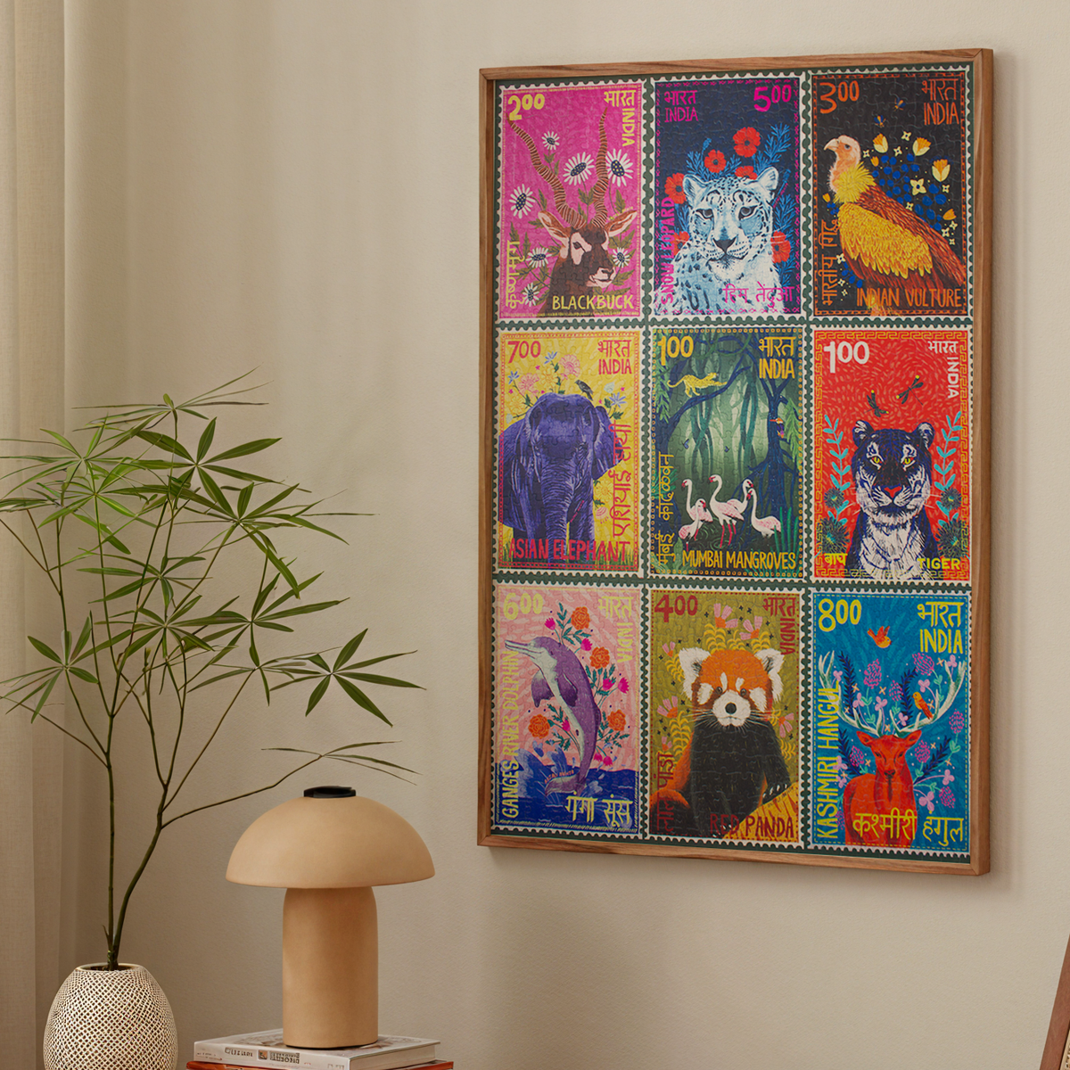 Colorful framed artwork of animal stamps on a wall above a wooden table with a lamp and books, next to a chair.