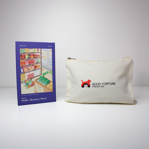A cream canvas cosmetic pouch with a gold zipper and the Good Fortune Press Co. logo, displayed next to its blue packaging box on a light gray background.